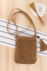 Detailed close-up of brown woven straw bag featuring fringe tassels and wood beads
