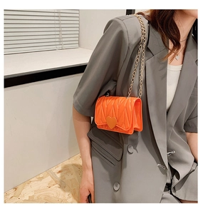 Close-up of bright orange mini chain bag with V-shaped quilting and heart buckle