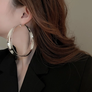 Close-up of large silver chunky hoop earrings worn by a model in a black blazer