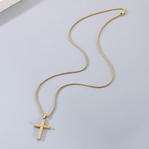 Détail d'un pendentif croix en acier doré sur une chaîne à mailles carrées polie