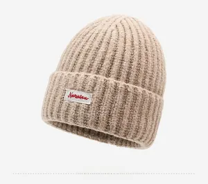 Dettaglio del berretto in maglia beige con trama a coste spesse e ricamo a lettere rosse