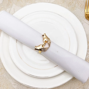 Close-up of golden heart-shaped hand gesture napkin ring on a white plate