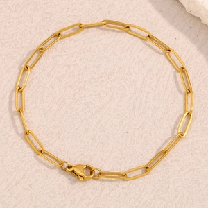 Detailed close-up of 18K gold-plated paperclip chain bracelet on beige textured surface