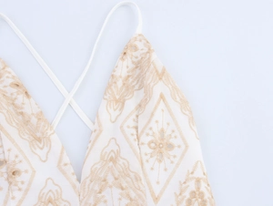Detailed view of V-neck white dress featuring gold bohemian embroidery and thin straps