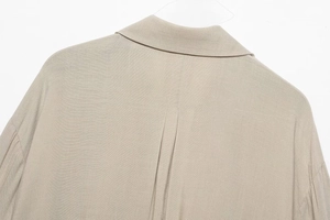 Detailed close-up of the shirt collar and back pleat design on khaki woven fabric