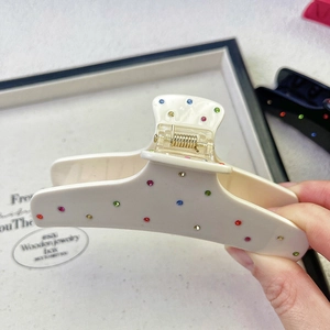 Detailed macro view of cream acetate hair claw clip with colorful rhinestones in hand