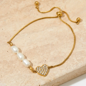 Adjustable gold pearl bracelet with heart cubic zirconia charm on a beige stone surface