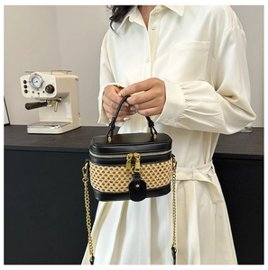 Detail of hand-held black leather and woven straw bucket bag with gold chain strap