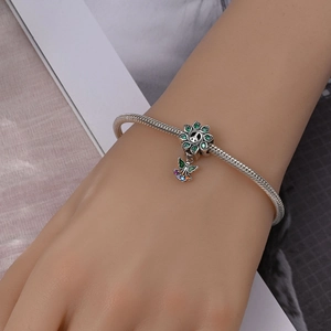 Detailed shot of silver snake chain bracelet with green flower and angel charms