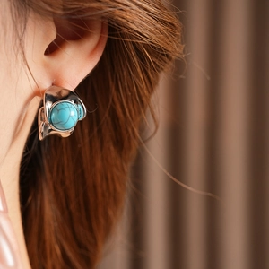Close-up of vintage C-shaped silver earring with round turquoise stone inlay on a model