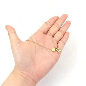 Detailed close-up of golden heart pendant and capital letter R charm on a dainty chain necklace