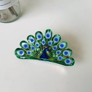 Detail shot of a peacock-shaped hair claw clip with emerald green and blue acetate finish