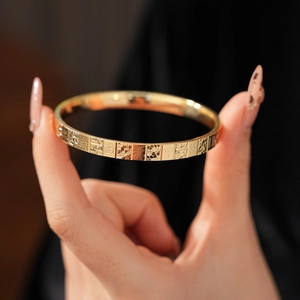 Close-up of golden mahjong bangles featuring engraved Chinese characters on a model hand