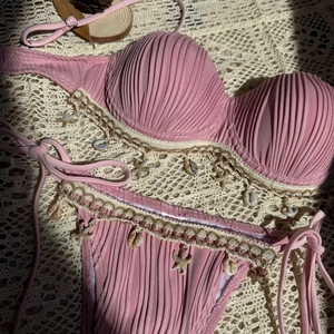 Detail of pink ribbed bikini set with seashell and starfish charms on a woven mat