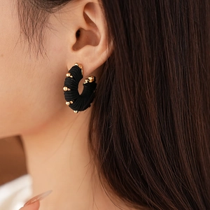 Close-up of black braided U-shaped earrings with gold beads on model ear