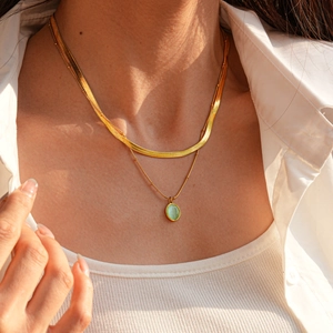 Détail de colliers superposés dorés avec un pendentif ovale en pierre verte élégante