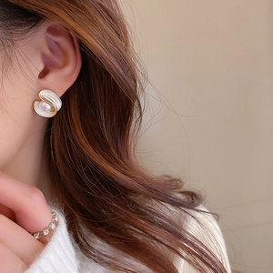 Close-up of shell shaped gold earrings with pearls worn by a model in soft lighting