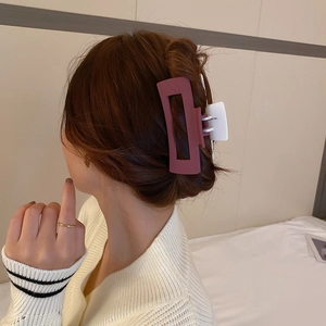 Détail d'une grande pince à cheveux marron rouge au design carré creux et ressort blanc