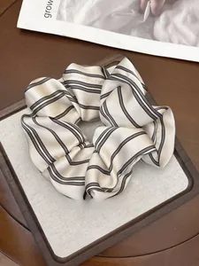Close-up of striped silk-like scrunchie in beige and black on a wooden tray
