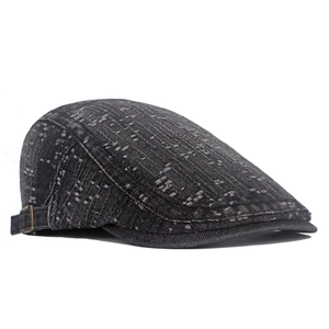 Detail of dark grey denim newsboy cap showing metal buckle and white textured stitching