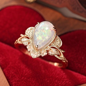 Macro detail of pear-cut opal ring with rose gold leaf motifs on red velvet