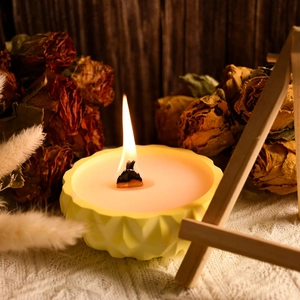 Detail showing a yellow geometric scented candle with a wooden wick in a cozy home setting