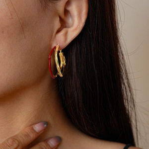 Dettaglio di orecchini a cerchio ondulati con finitura in oro 18k e smalto rosso su modella