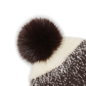 Detail of winter knitted hat featuring a fluffy brown faux fur pompom and jacquard pattern