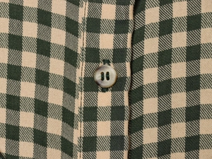 Macro detail of green and beige gingham woven fabric with a dark four-hole round button
