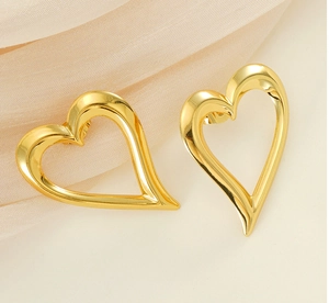 Close-up of polished gold hollow heart-shaped stud earrings on soft silk fabric