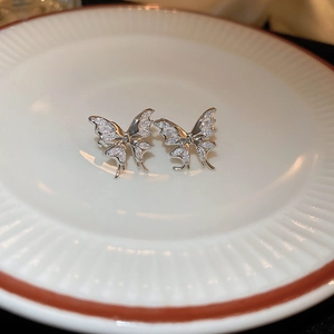 Silver butterfly ear clips with cubic zirconia on a white ceramic plate for women