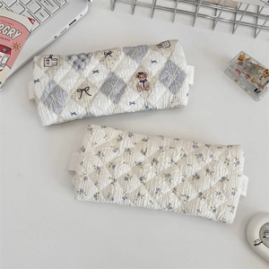 Detail of quilted floral and bear plaid pencil cases with lace trim on a white desk