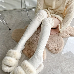 Detail of white vertical knit over-the-knee socks paired with plush slippers