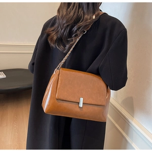 Brown leather crossbody bag with silver buckle and chain strap on a black coat