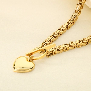 Macro detail of gold king chain with heart pendant and OT toggle clasp on beige fabric