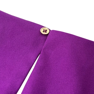 Detail of purple crepe dress featuring a polished gold four-hole button and textured fabric