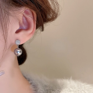 Close-up of a silver pearl earring with sparkling zircons worn by a model on a beige background