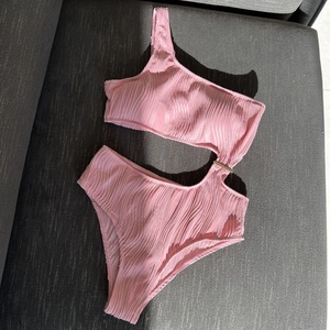 Pink one-shoulder swimsuit detail with ribbed fabric and golden metal buckle decoration