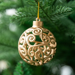 Hollow gold Christmas ball ornament with scroll patterns hanging on a pine tree