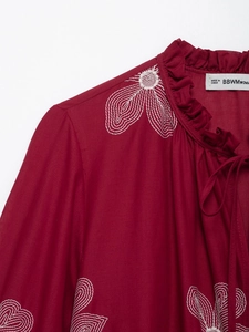 Detail of raspberry embroidered shirt with ruffle collar and white floral patterns