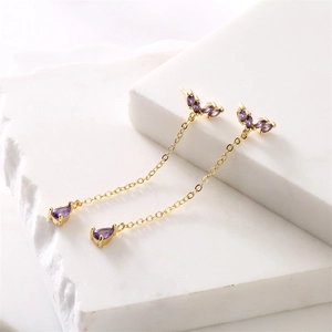 Detail of gold fringe earrings with purple stones on white stone steps background