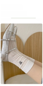 Detail of white ribbed crew socks with black embroidery paired with silver Mary Jane shoes