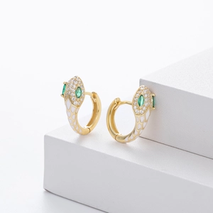 Detail of gold snake huggie earrings with white enamel and green gemstone eyes