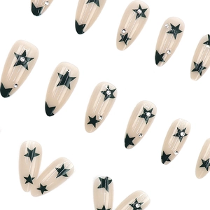 Almond-shaped press-on nails with nude base, black stars, and sparkling rhinestones