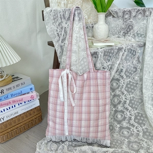 Detailed view of pink plaid tote bag with delicate white lace trim and bow on a wooden chair
