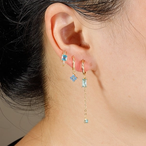 Detailed view of three gold-plated earrings with blue zircon stones worn on the ear