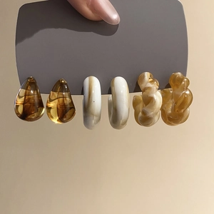 Close-up of acrylic C-shaped earrings in amber and marble patterns on a display card