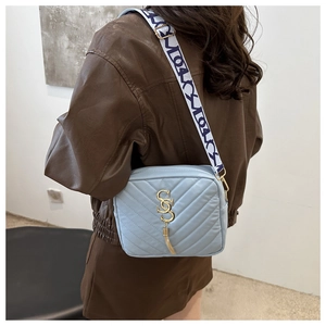 Detail of light blue quilted crossbody bag with wide logo strap and gold hardware