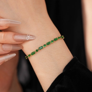 Detailed close-up of gold-plated bracelet with emerald green stones on model's wrist