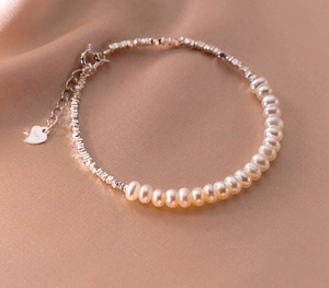 Detail of S925 silver necklace with white pearls and heart pendant on soft satin
